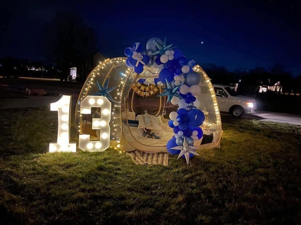 Nighttime backyard bubble tent glowing with fairy lights, a lit '13' marquee and a blue star balloon arch. Children's Birthday Parties by EPIC Parties in Middle Tennessee.
