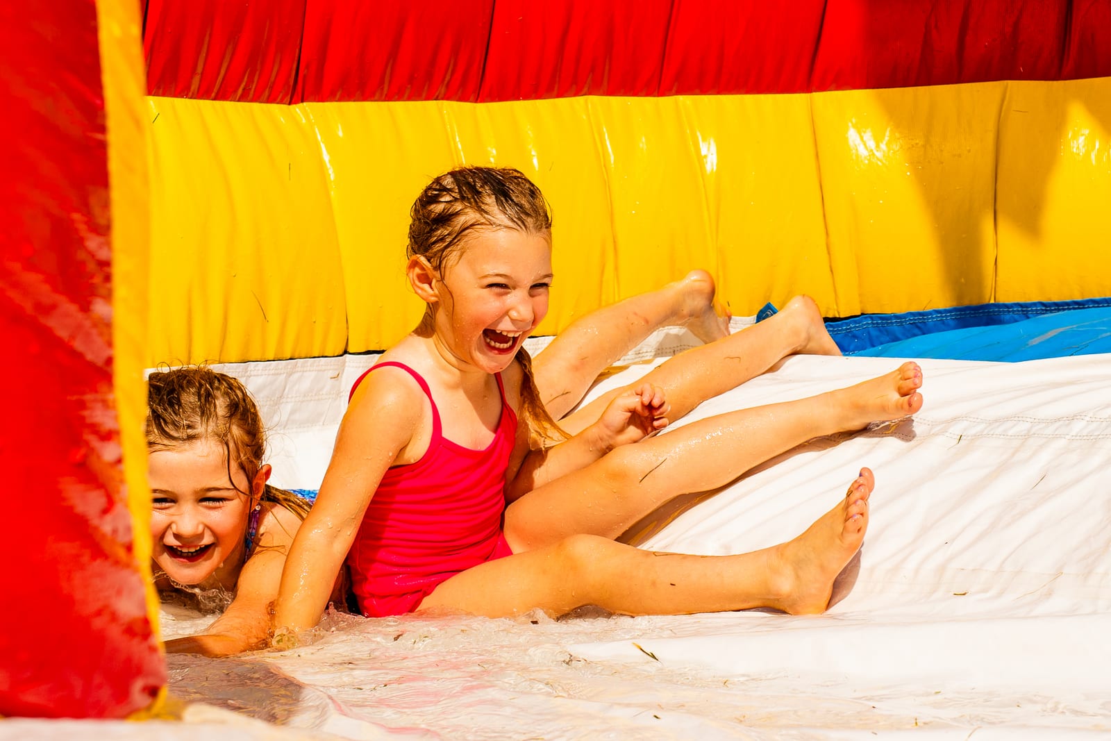 Two children laughing mid-slide on a colourful inflatable water slide