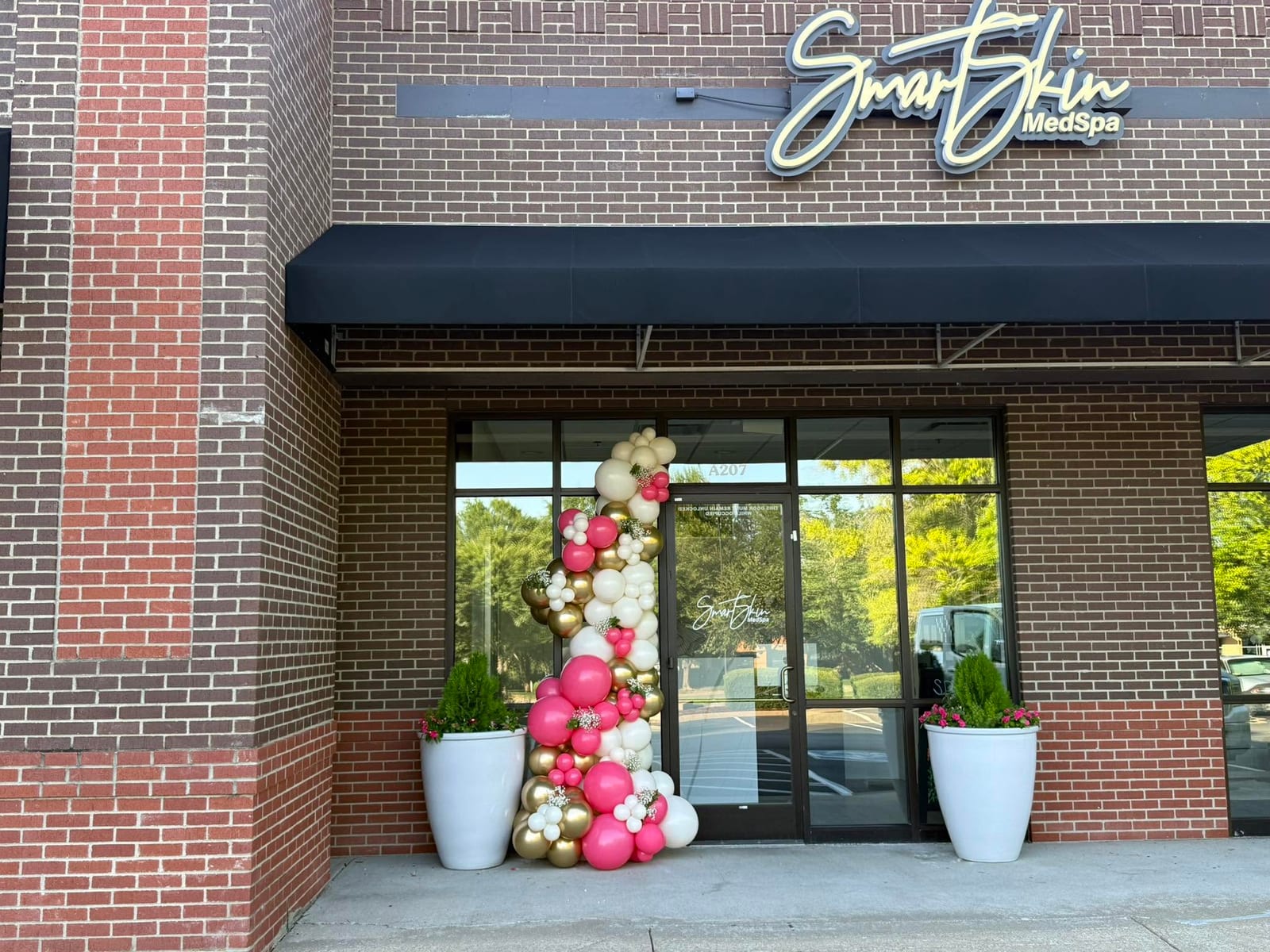 Brick storefront with a pink and white balloon garland arching over the entrance on opening day. Grand Openings by EPIC Parties in Middle Tennessee.