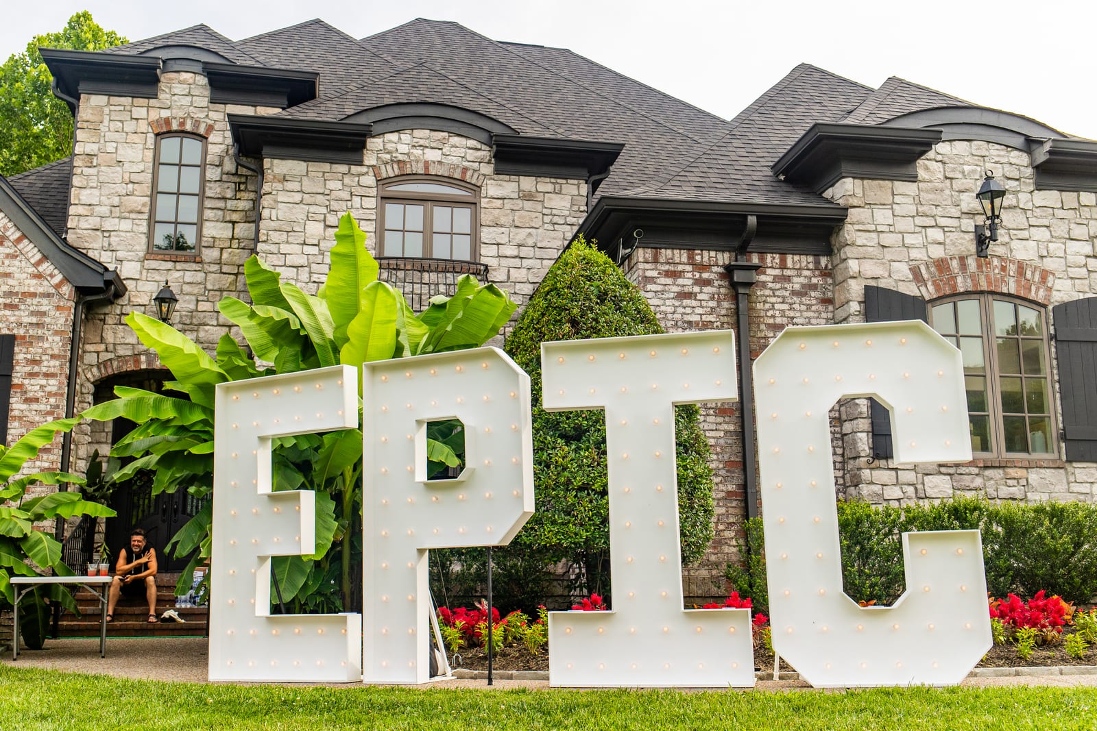 Giant illuminated EPIC marquee letters standing on a lawn in front of a stone house